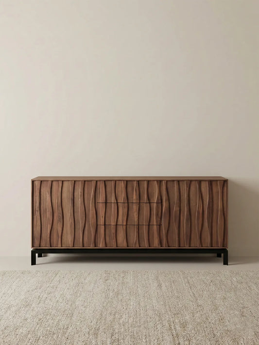 Front view of Walnutry Suiseki 71 inch solid walnut sideboard featuring vertical sculptural wave door panels and black base against a minimal beige wall.