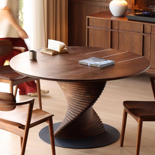 Round North American Black Walnut dining table with sculpted spiral base, open book and magazine on top, matching wooden chairs in modern room