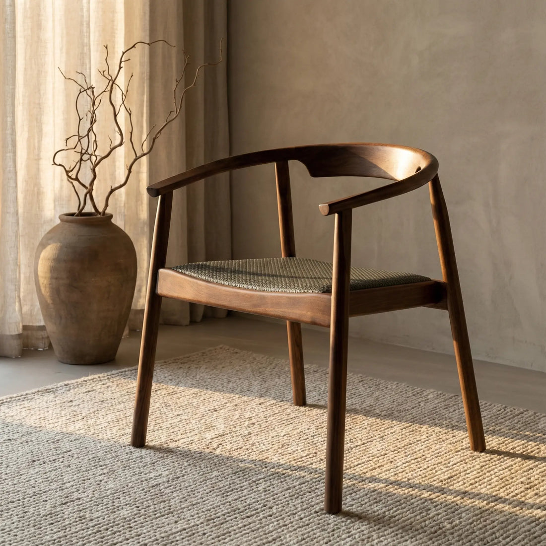 Modern solid black walnut armchair with woven fabric seat on beige rug near large ceramic vase with dried branches