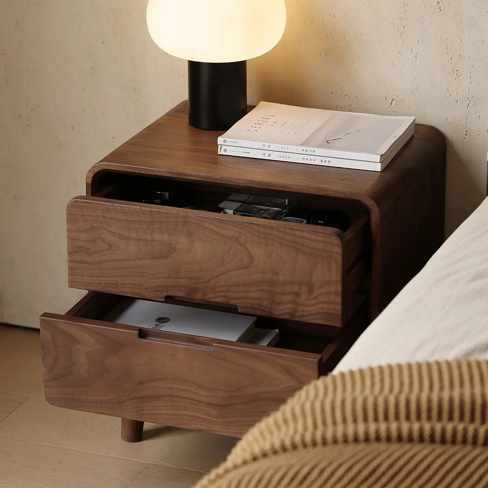 Solid walnut nightstand with two open drawers, lamp, and magazines on top in cozy bedroom