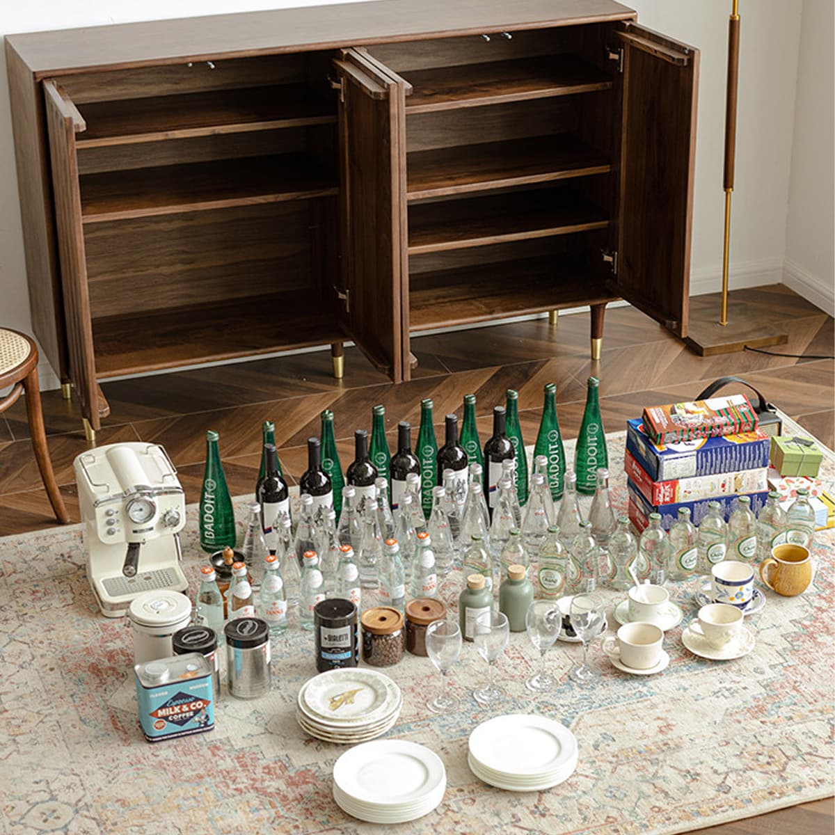 Open solid black walnut cabinet with brass feet on herringbone wood floor, surrounded by glass bottles, cups, plates, and coffee items on patterned rug