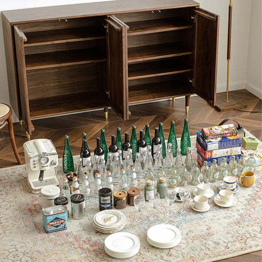 Open solid black walnut cabinet with brass feet on herringbone wood floor, surrounded by glass bottles, cups, plates, and coffee items on patterned rug