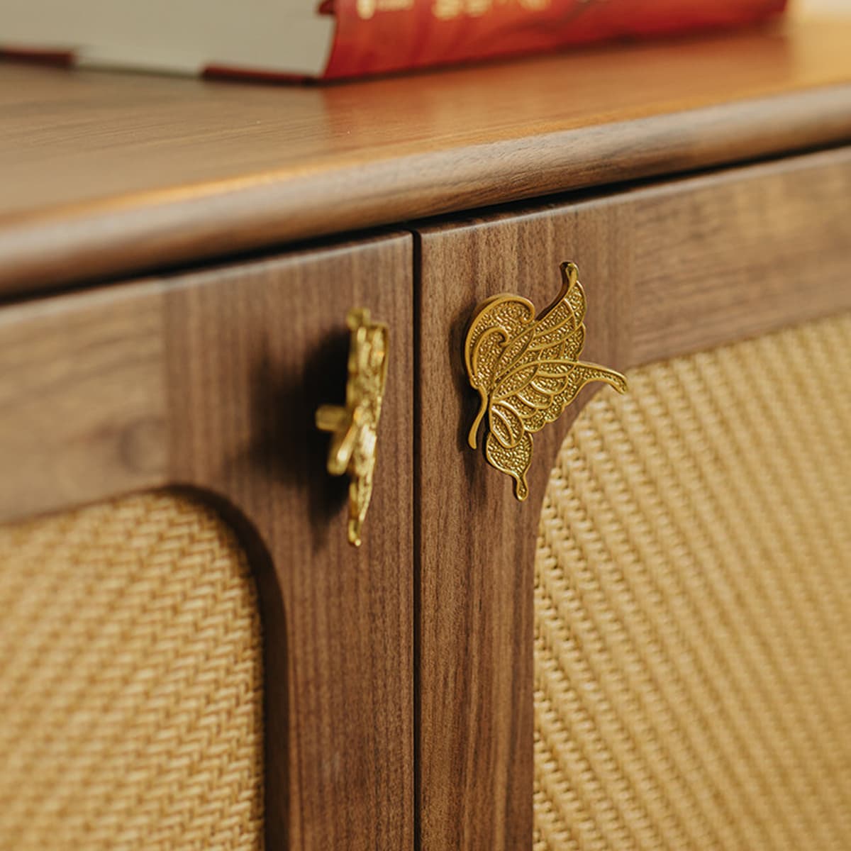 Close-up of walnut wood cabinet with woven rattan panels and gold butterfly-shaped handles
