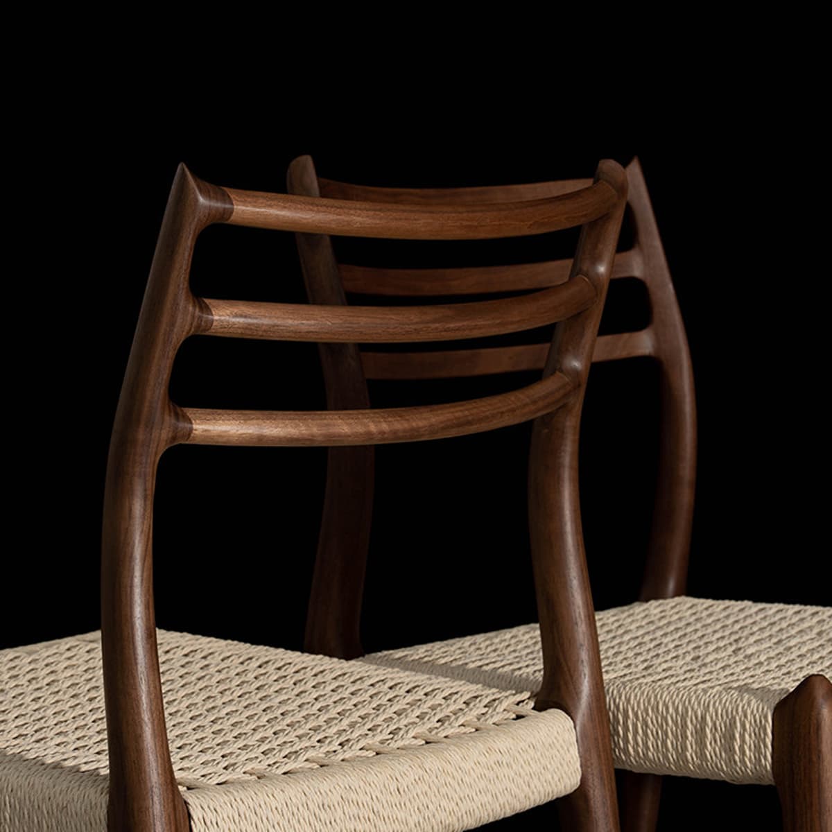 Close-up of two handcrafted solid North American black walnut chairs with woven natural fiber seats against black background