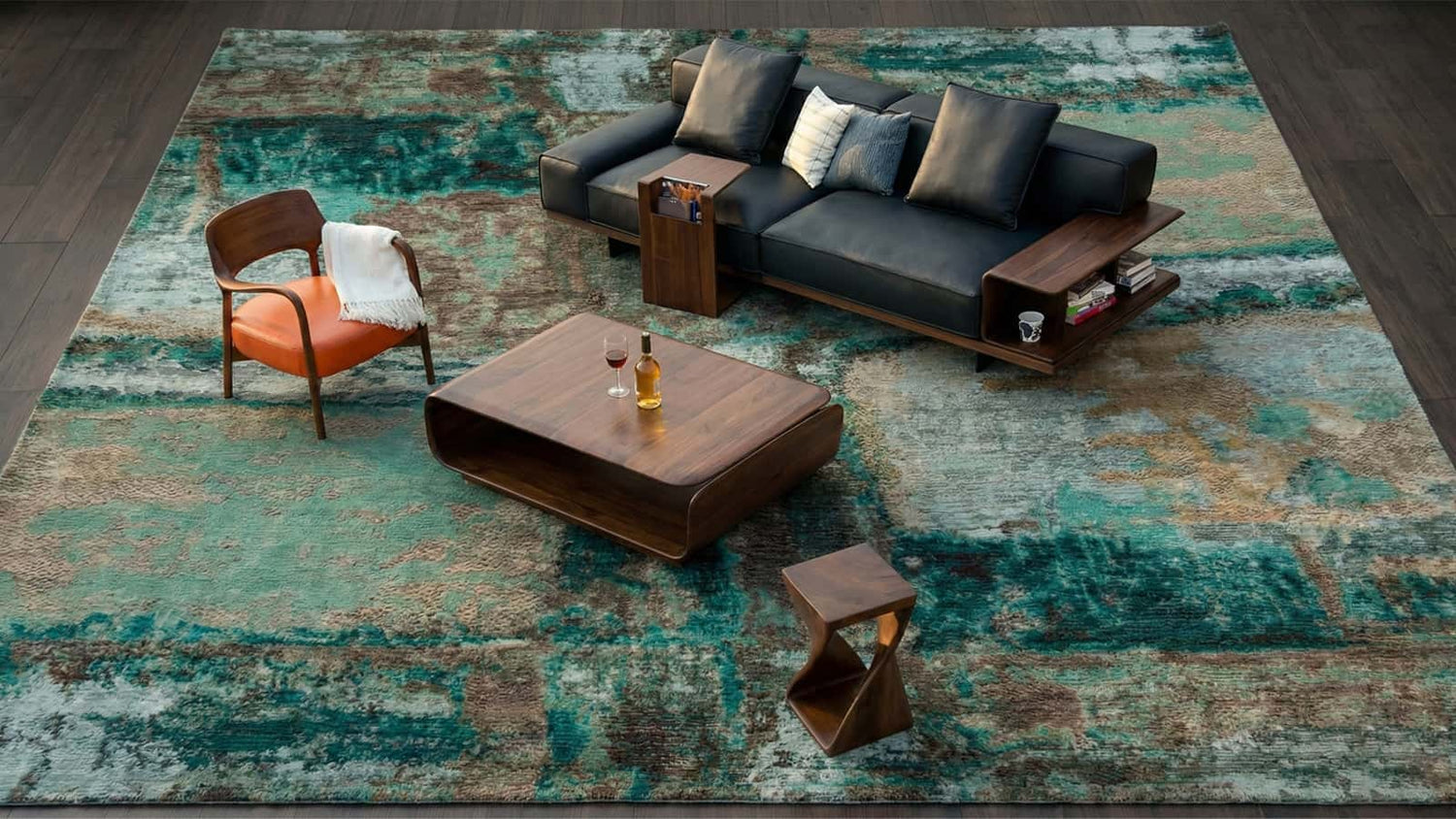 Top-down view of a contemporary living room furniture set featuring a black leather sofa with walnut side tables, a wooden coffee table, an orange accent chair, and a twisted wood stool on a large teal rug.