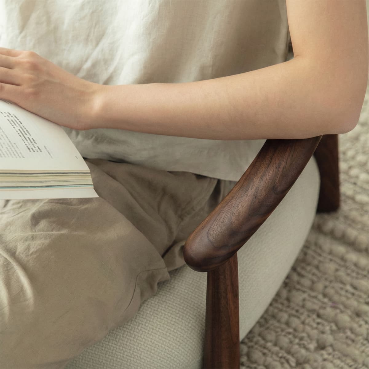 Close-up of person reading book while sitting on a chair with solid North American Black Walnut armrest
