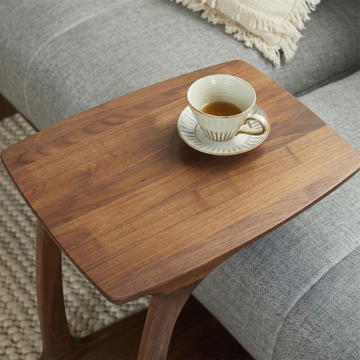 Close-up top view of the Walnutry Helios C-table, showcasing the rich grain and texture of the solid walnut wood surface with a teacup placed on it.