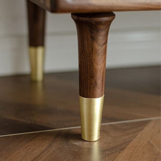 Close-up of solid North American black walnut furniture leg with brass cap on wooden floor