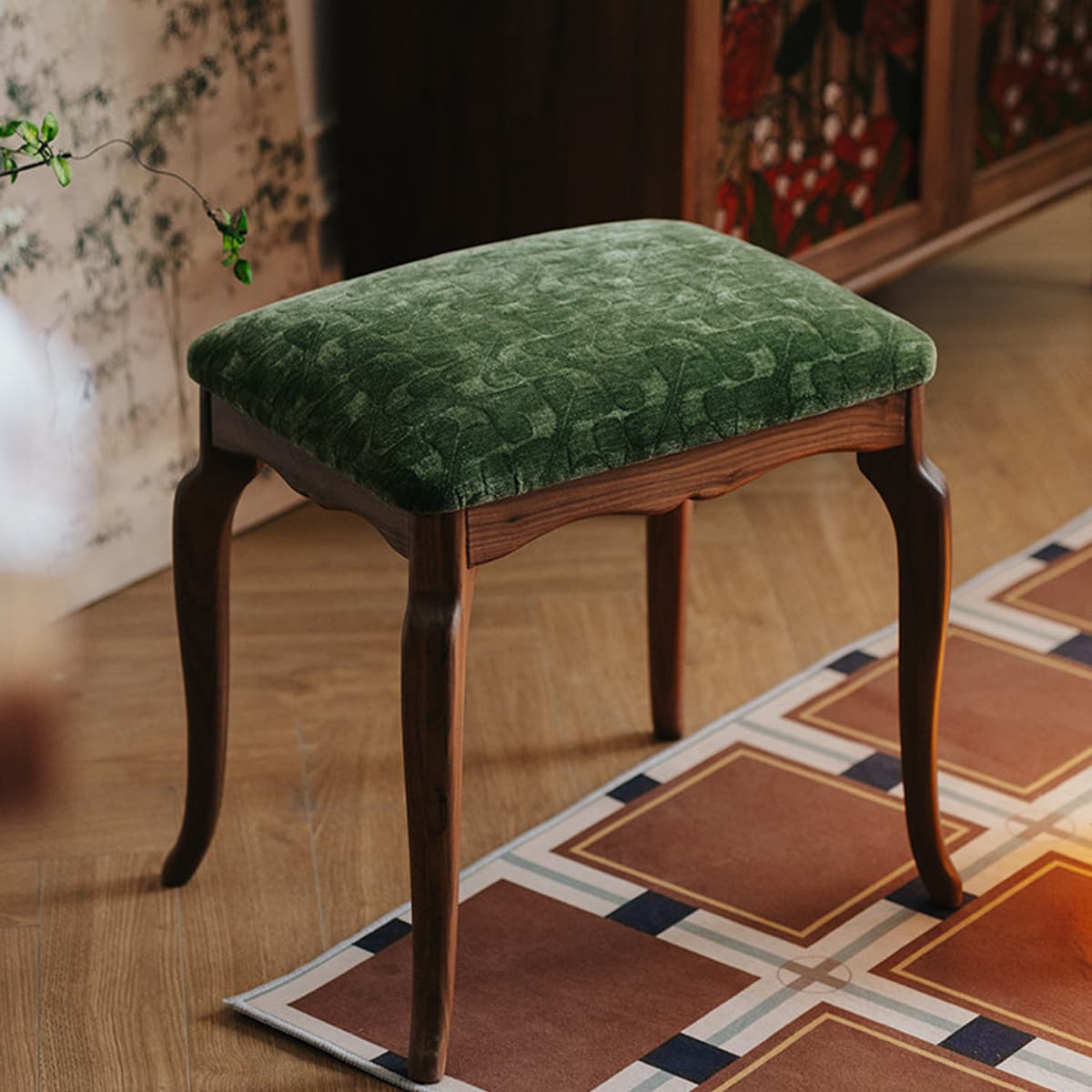 Heirloom-quality solid black walnut stool with green textured cushion on wood floor and patterned rug