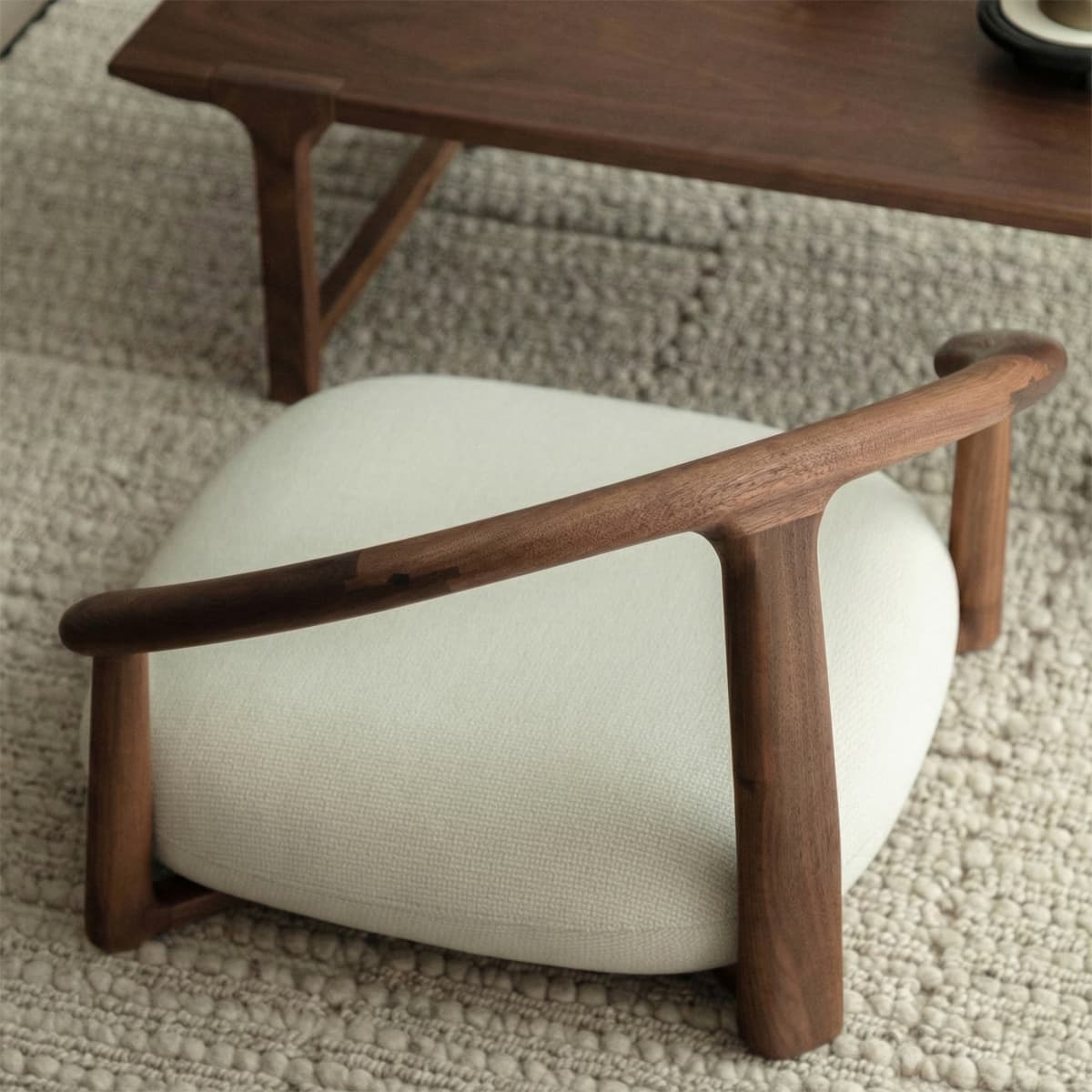 Solid black walnut wood low chair with curved armrest and white cushioned seat on textured rug