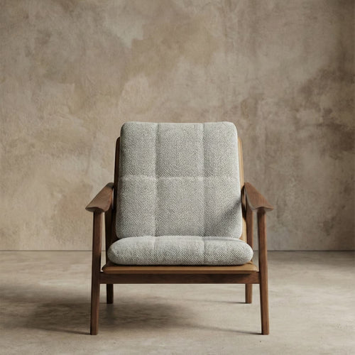 Mid-century modern lounge chair with black walnut frame and gray herringbone cushion against textured beige wall