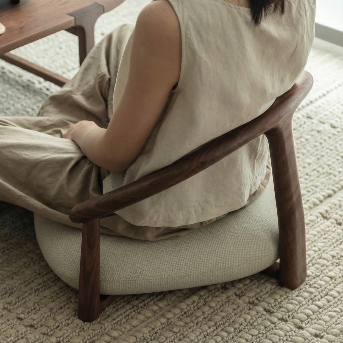 Person seated on a solid black walnut wooden chair with curved backrest and beige cushion on textured rug