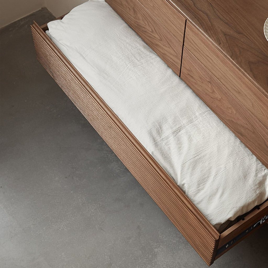 Open wooden drawer with textured front panel holding folded white linen on a concrete floor