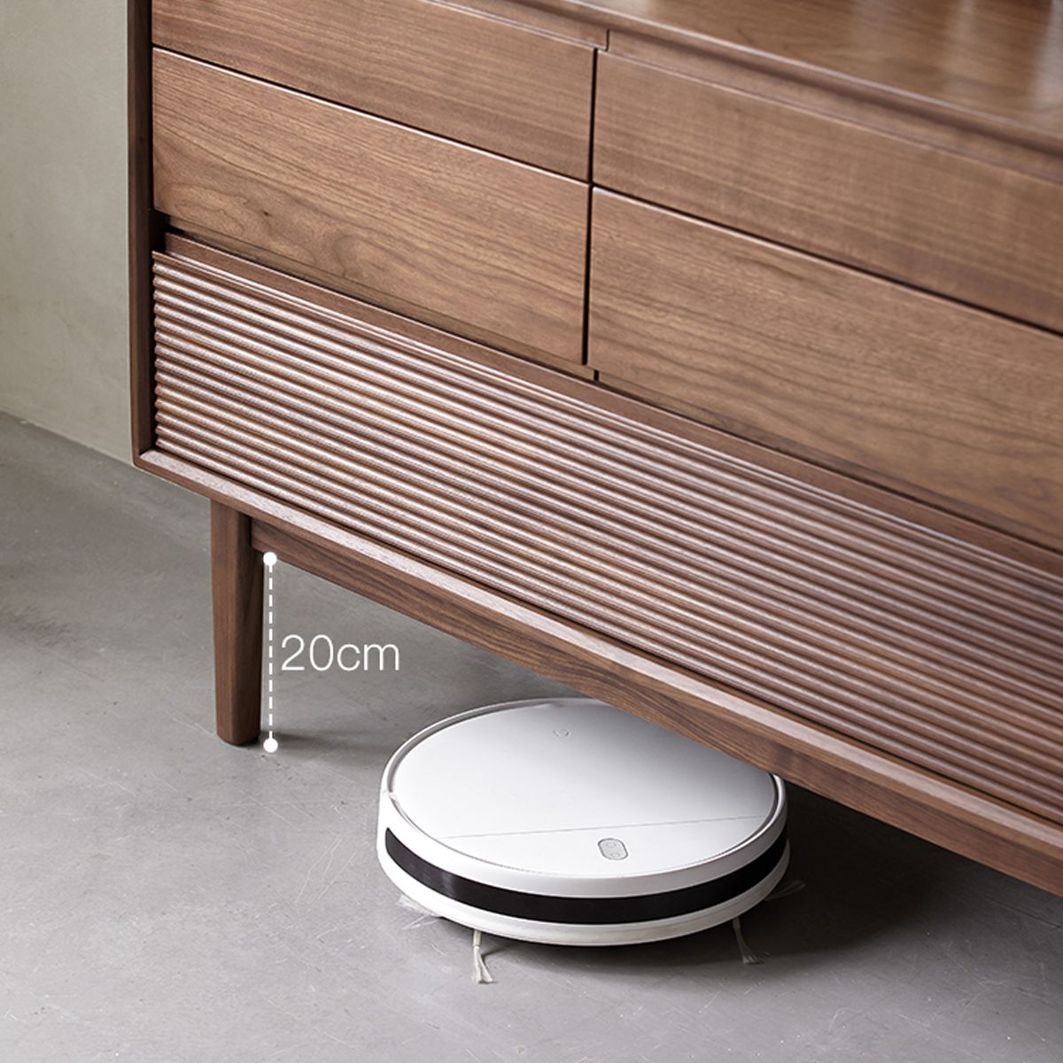 White robotic vacuum cleaner under wooden textured drawer measuring 20cm clearance on concrete floor