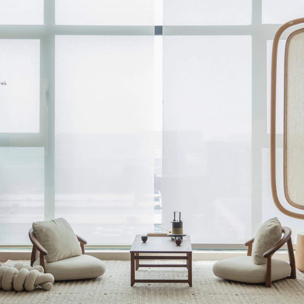 Minimalist living room with two beige cushioned walnut wood chairs and a walnut wood coffee table on woven rug