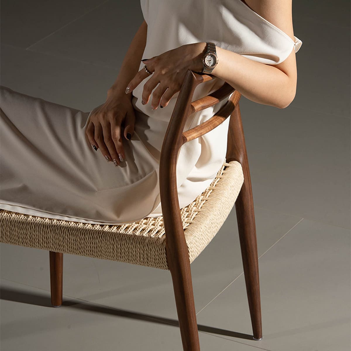 Woman in beige dress seated on a solid black walnut chair with woven seat and curved backrest in modern room