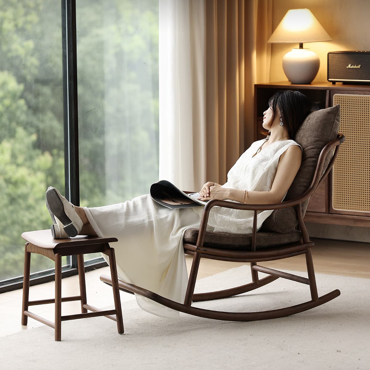Woman relaxing in solid walnut rocking chair with cushion and matching footrest near large window