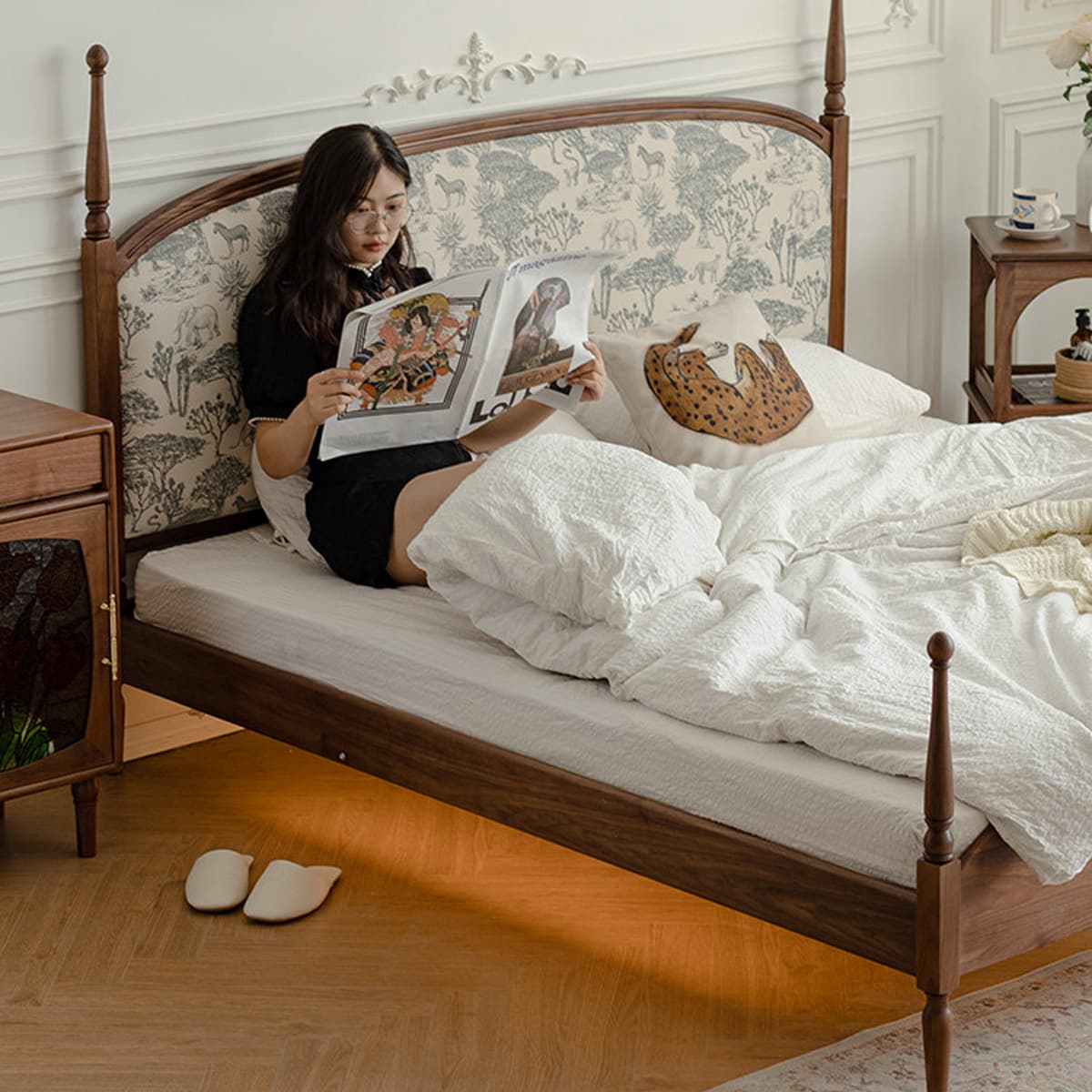 Woman reading magazine on a solid black walnut bed with upholstered animal print headboard and white bedding