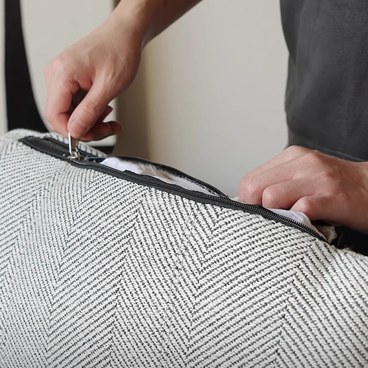 Hands unzipping textured gray and white herringbone pillow cover showing inner cushion