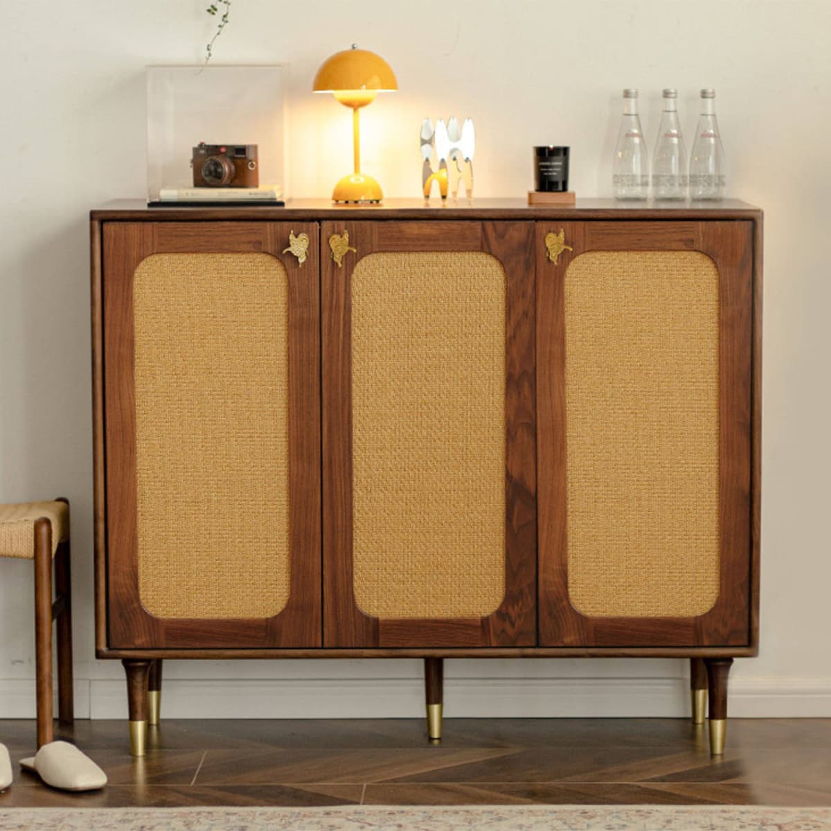 Solid walnut cabinet with woven rattan inset doors and brass hardware, styled with decorative items and a yellow lamp