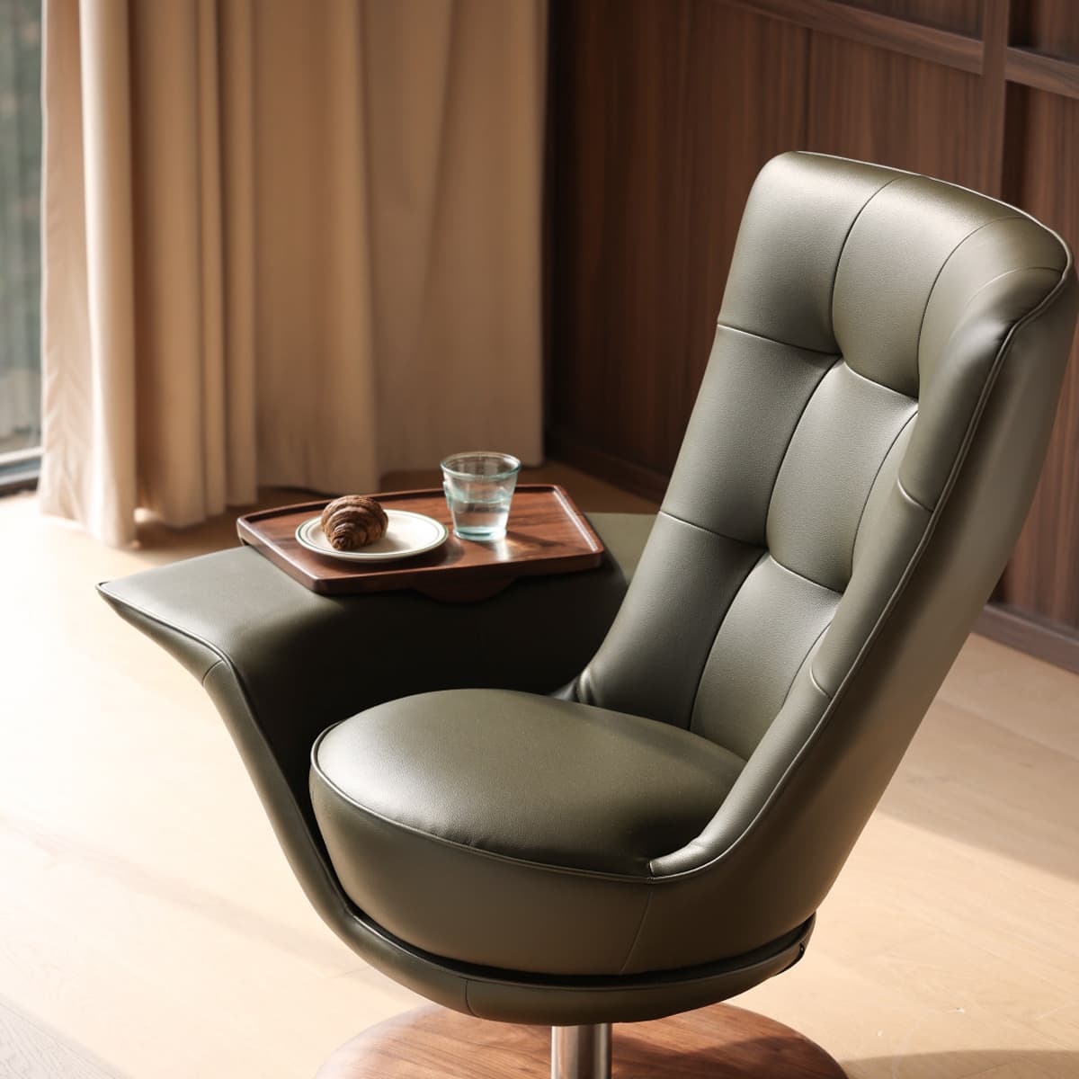 Modern leather lounge chair with attached wooden tray holding croissant and glass of water, in warm room