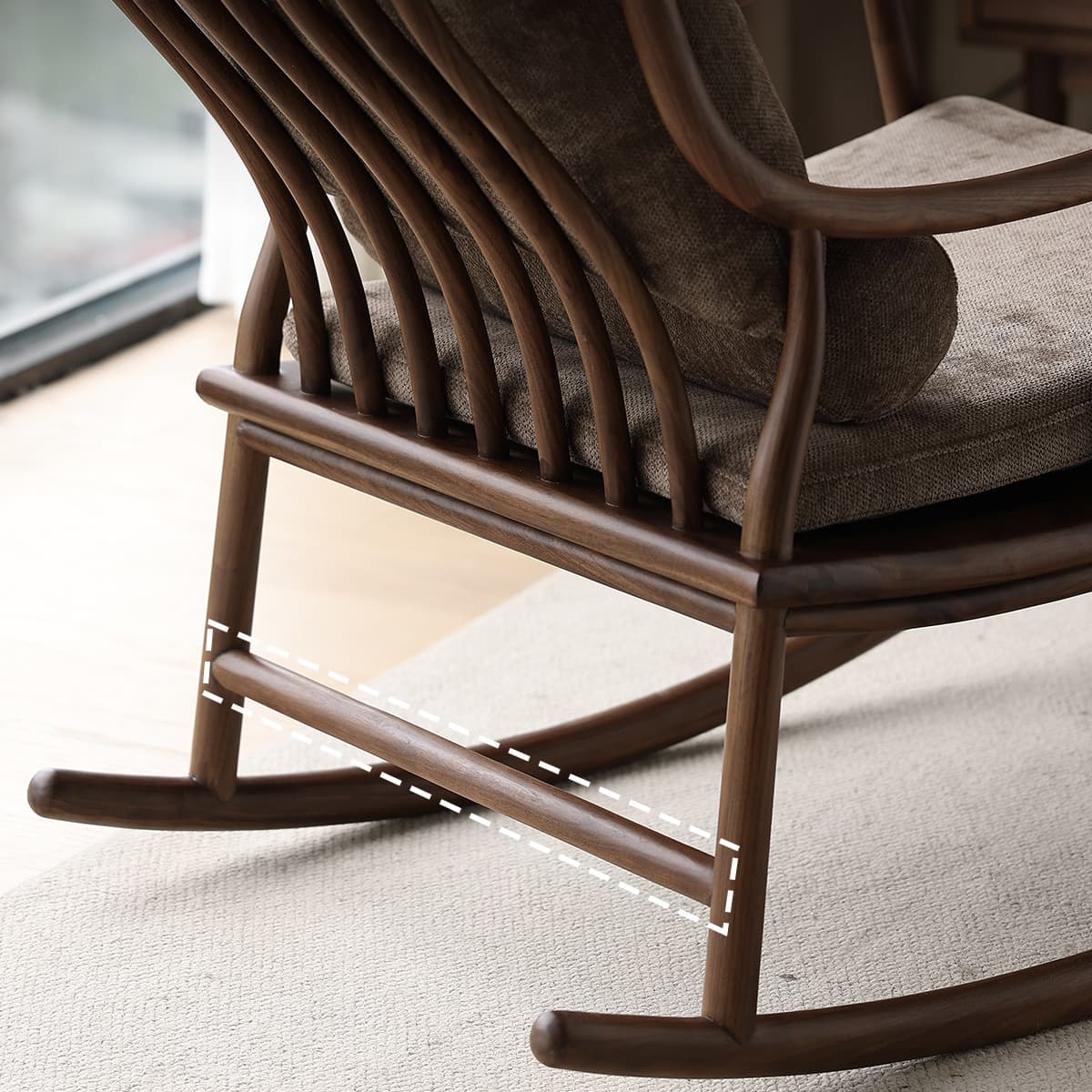 Close-up of a solid North American black walnut rocking chair with textured gray cushions on a beige rug by a window