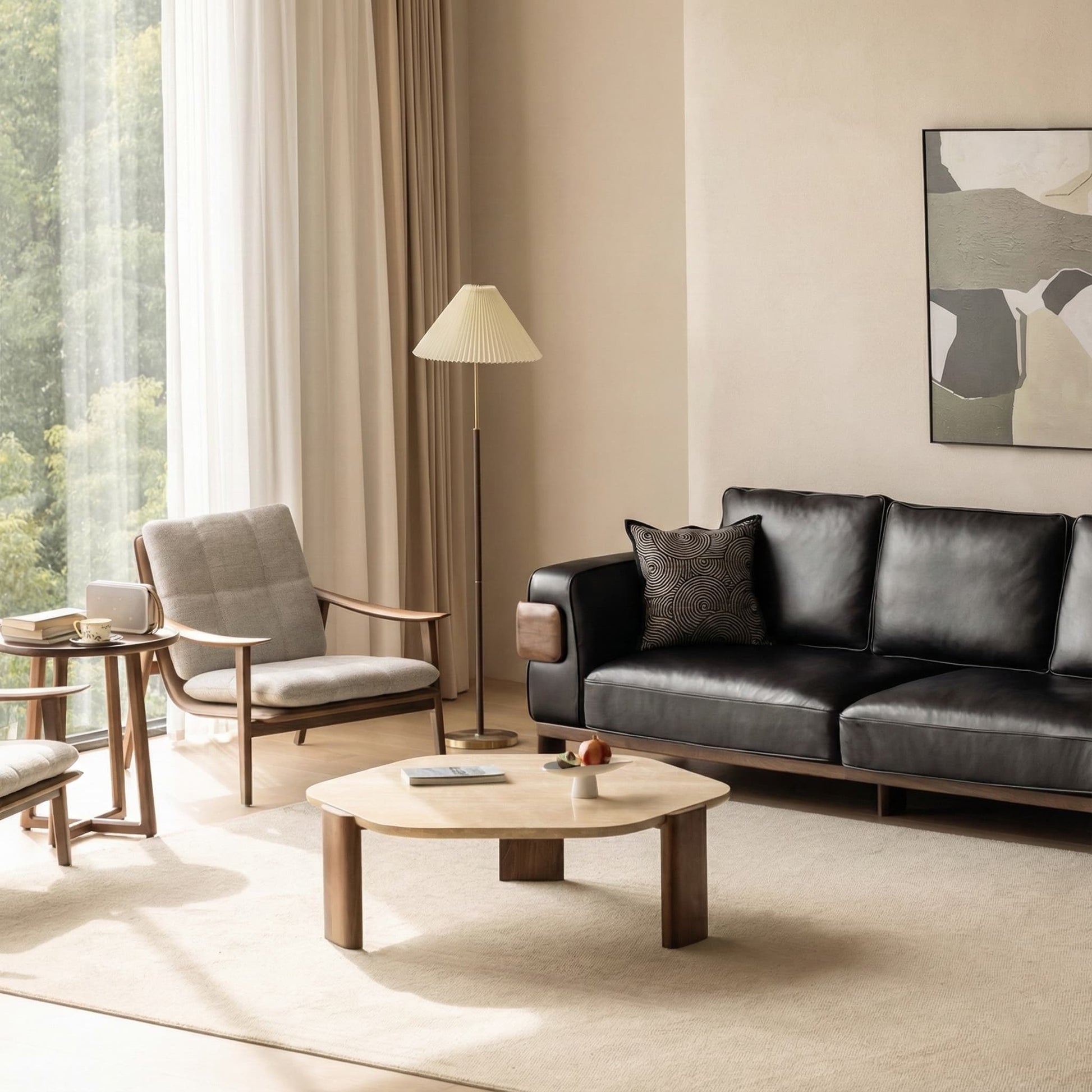 Modern living room with black leather sofa, beige cushioned wood armchair, wooden coffee and side tables, floor lamp, and abstract wall art