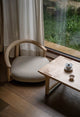 Zen-style low wooden lounge chair and tea table set by a large window overlooking a rainy garden, featuring a traditional tea set.