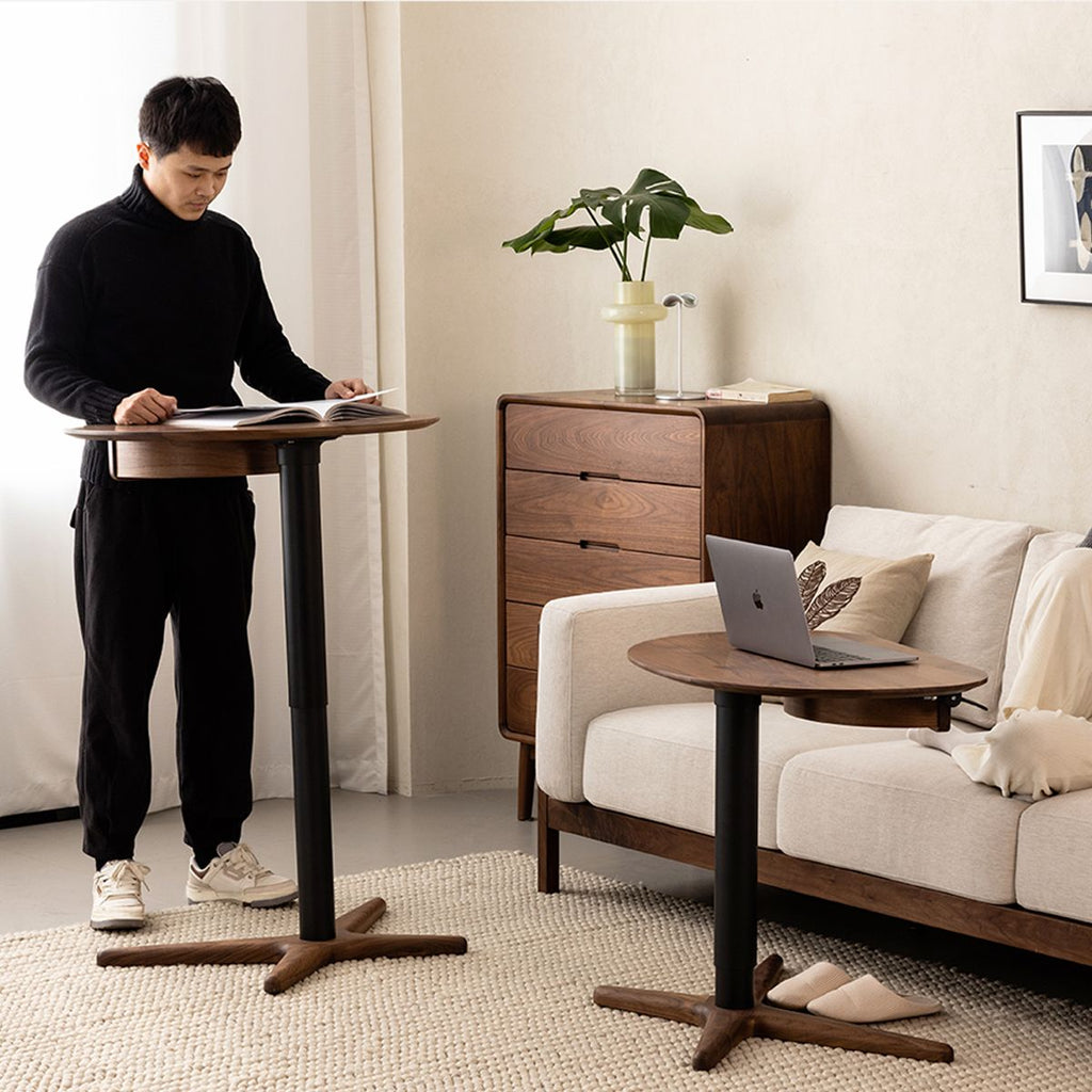 Modern adjustable height walnut side tables in cozy living room with man reading and laptop on sofa