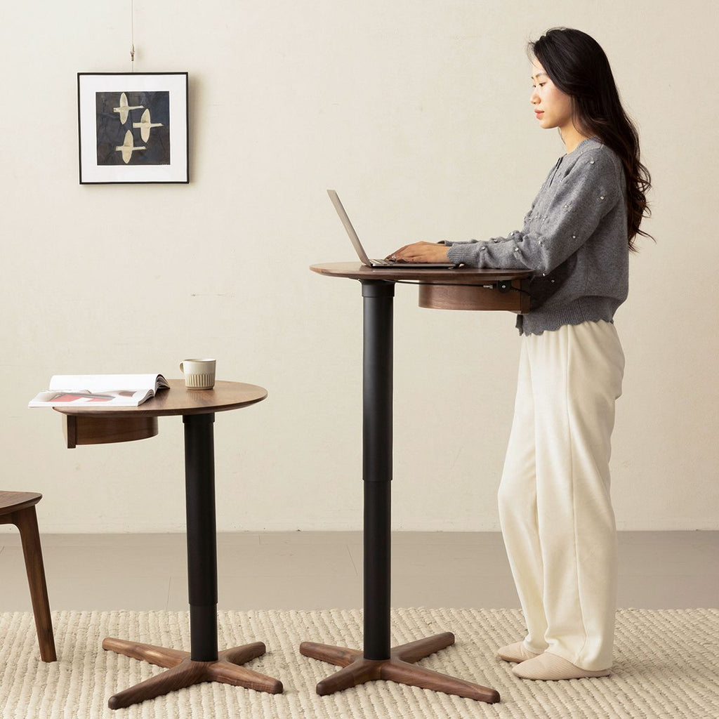 Woman using adjustable height walnut side table as standing desk in minimalist room with artwork