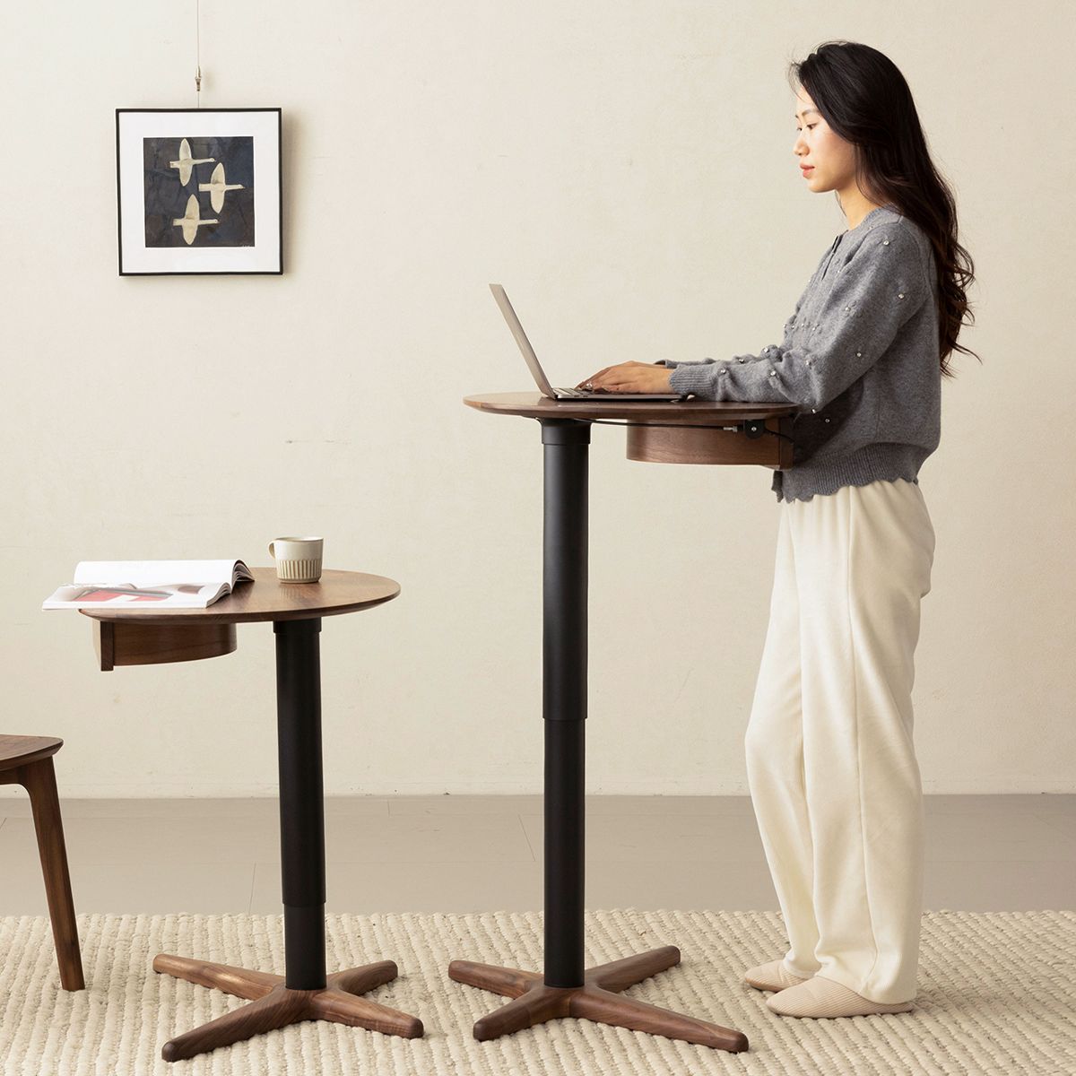 Woman using adjustable height walnut side table as standing desk in minimalist room with artwork