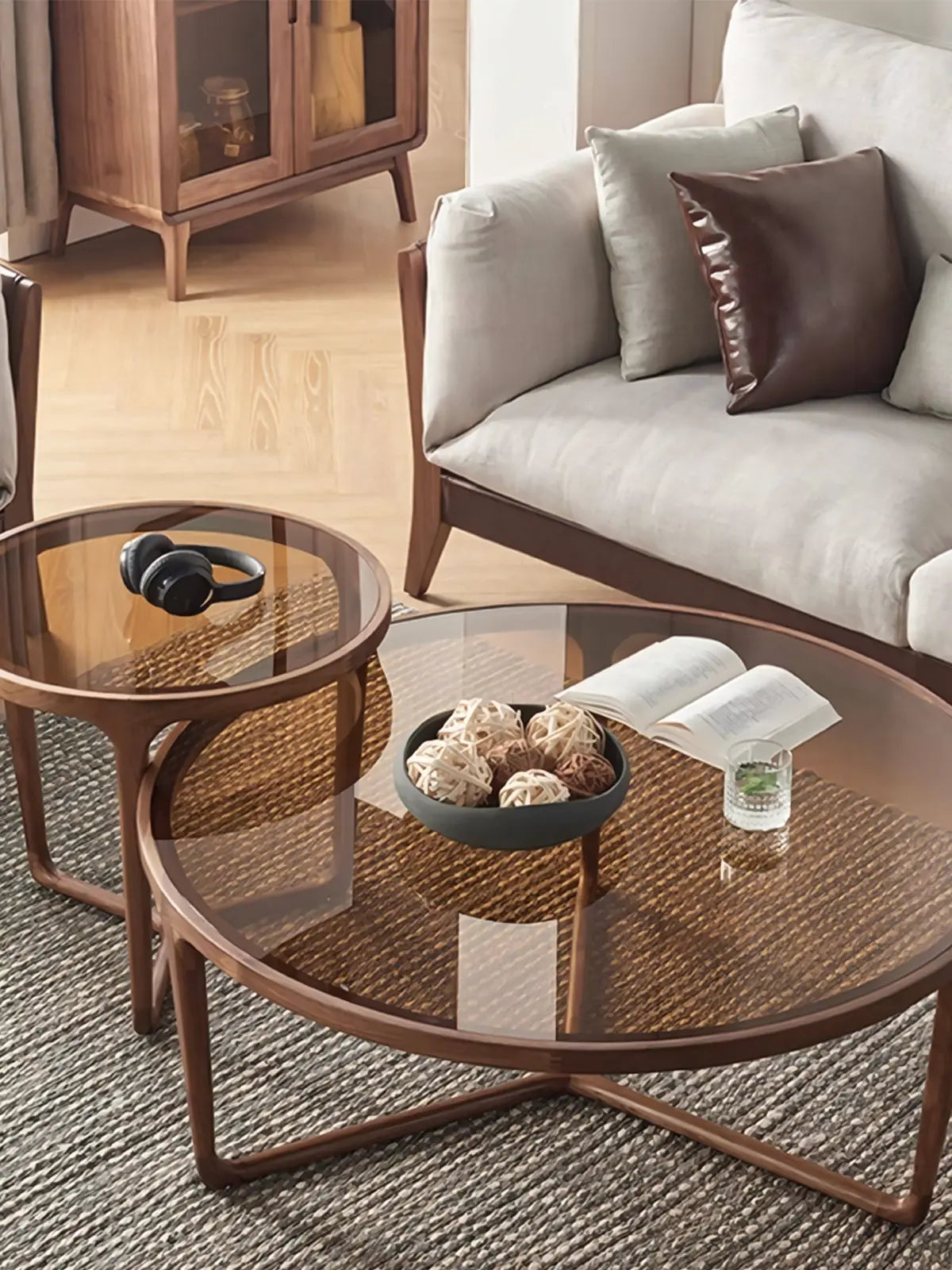 The Solstice nesting tables styled in a sunlit mid-century modern living room, featuring a beige sofa and the warm glow of the amber glass top contrasting with the dark walnut wood.