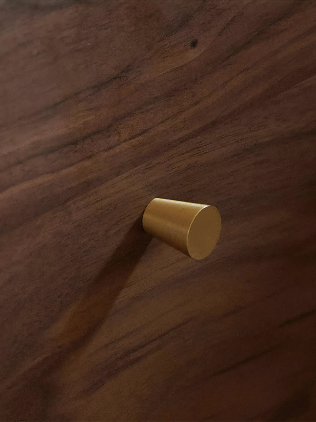 Macro detail of brushed antique brass hardware knob contrasting against dark American black walnut grain.