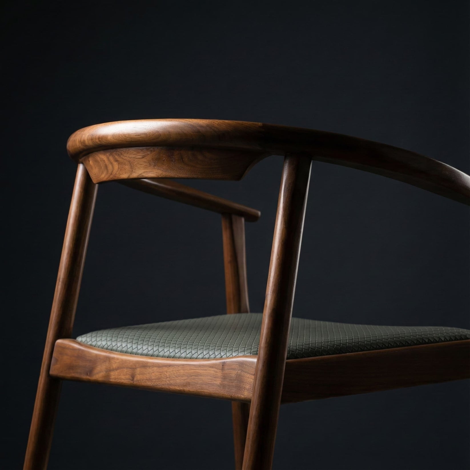 Close-up of a wooden chair with curved backrest and textured green seat against black background