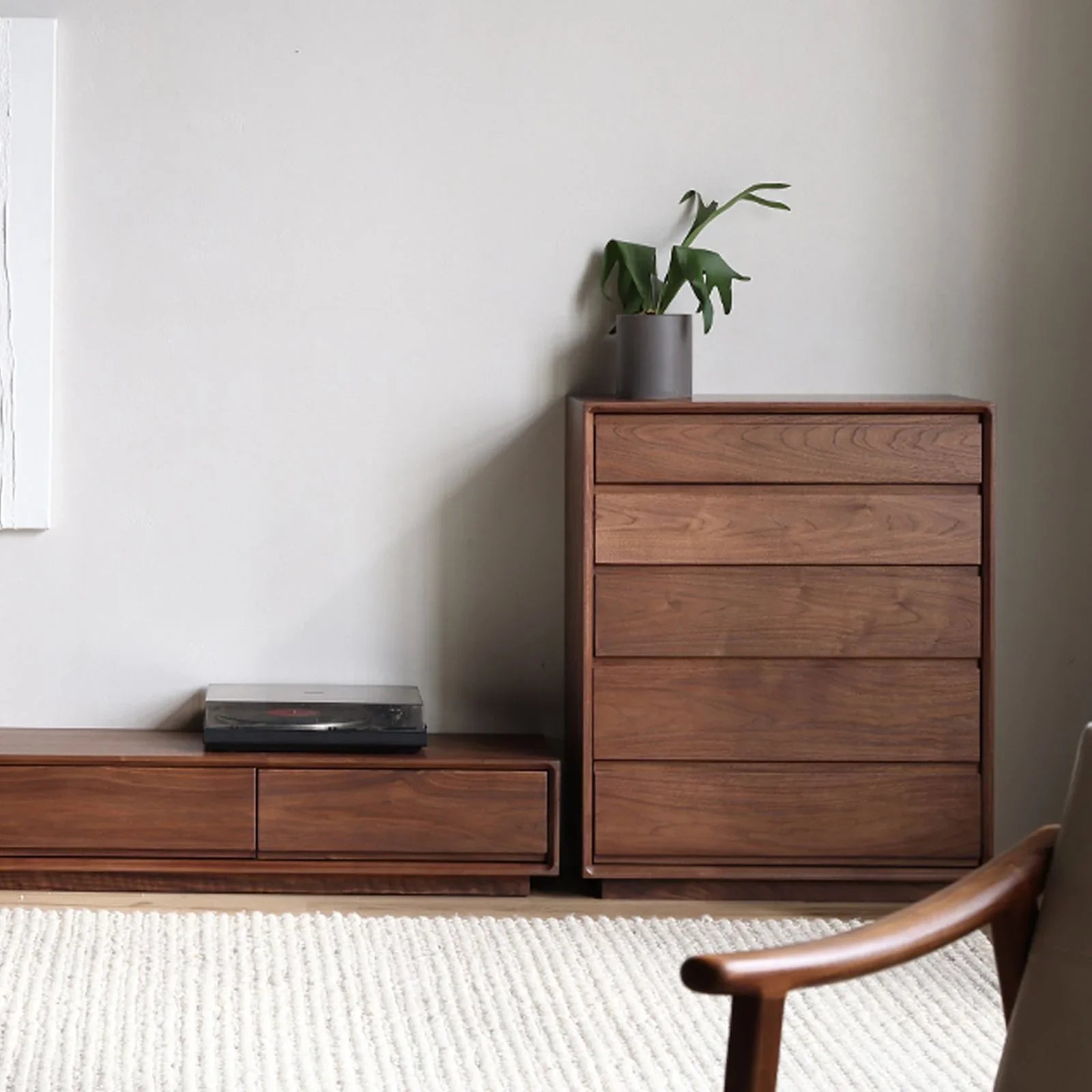 Solid black walnut bedroom corner with a five-drawer chest, low cabinet, and potted plant