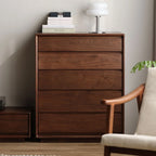 Solid wood bedroom chest of drawers with books and modern white lamp on top, next to wooden armchair