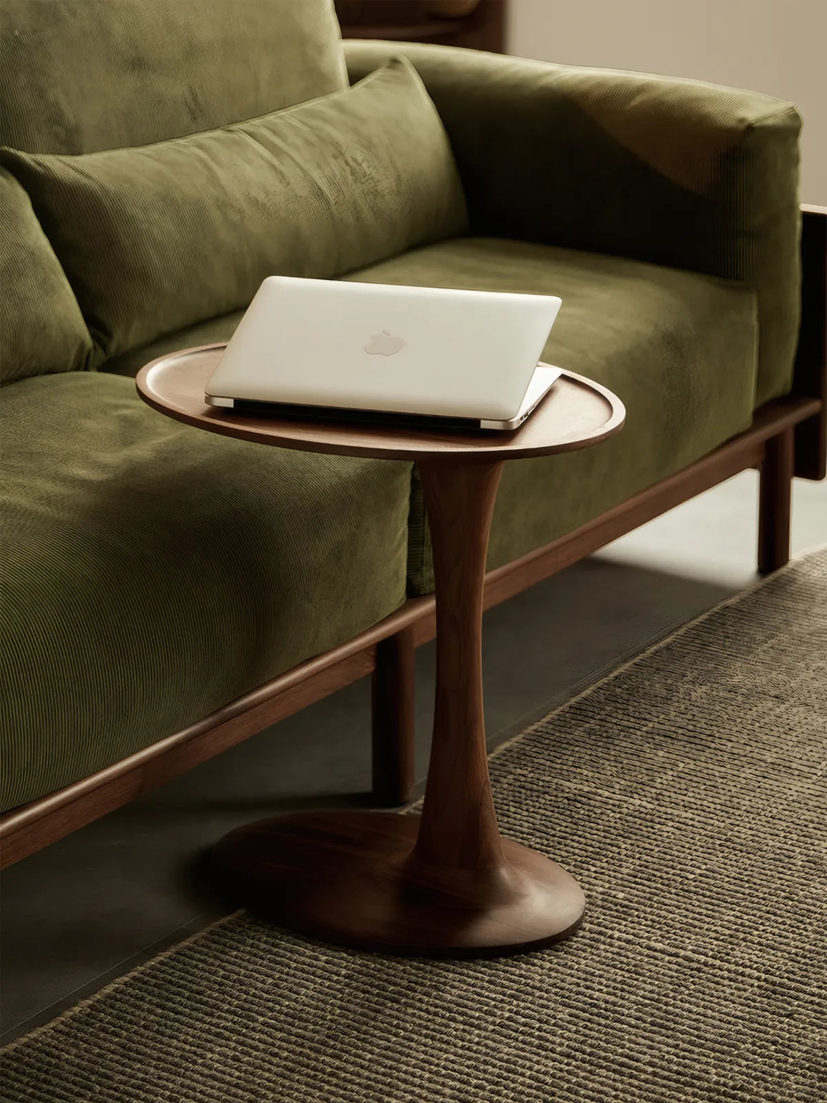 The Orbit solid walnut table positioned next to a green velvet sofa holding a laptop, functioning as a stylish work-from-home station.
