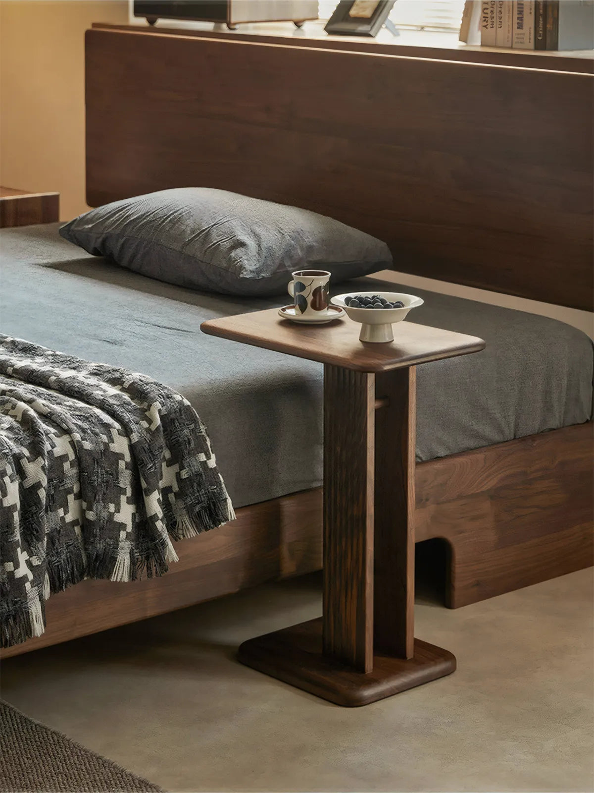 Versatile usage of the Meridian walnut table as a minimalist nightstand next to a bed, showcasing its ability to slide under furniture.