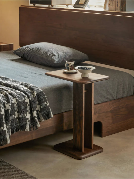 Versatile usage of the Meridian walnut table as a minimalist nightstand next to a bed, showcasing its ability to slide under furniture.