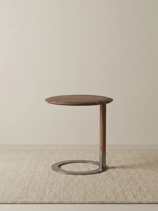 Low angle view of the C-table showing the weighted metal ring base and solid walnut stem on a textured rug.