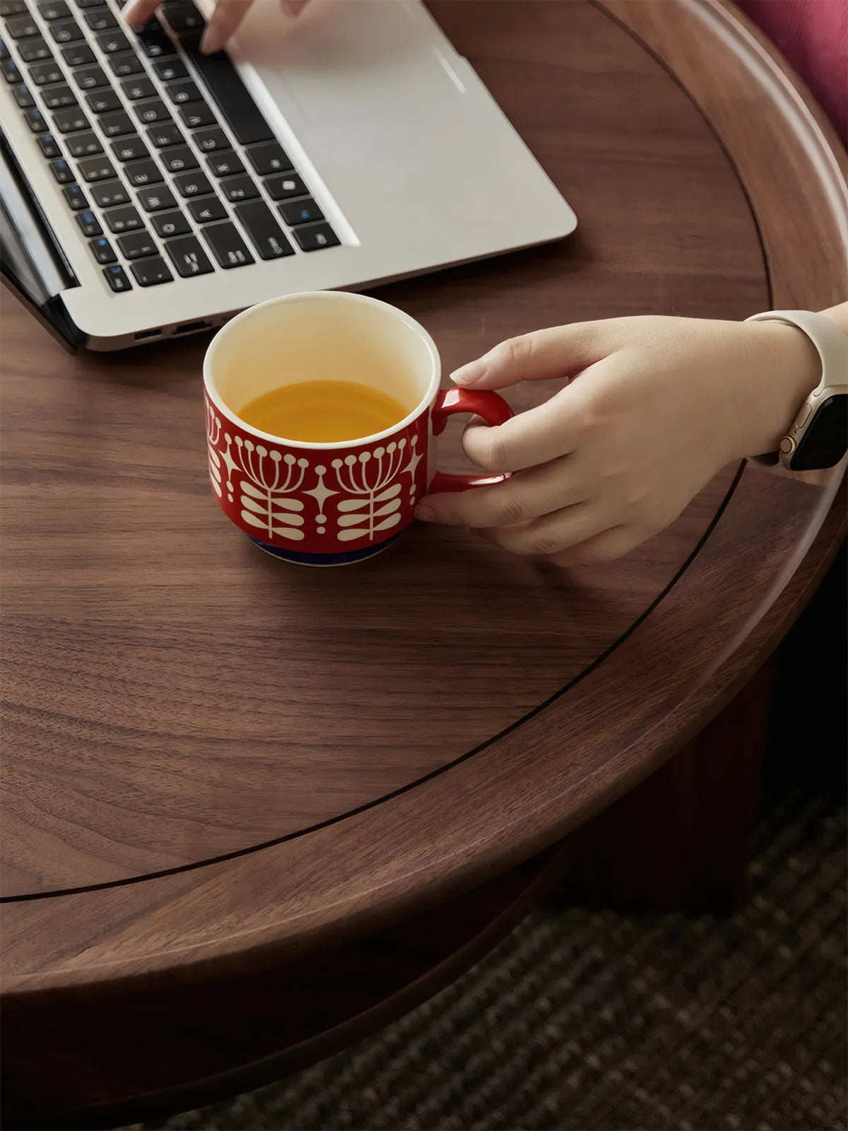 User placing a red coffee cup on the smooth matte finish of the solid walnut round table, showing scale.