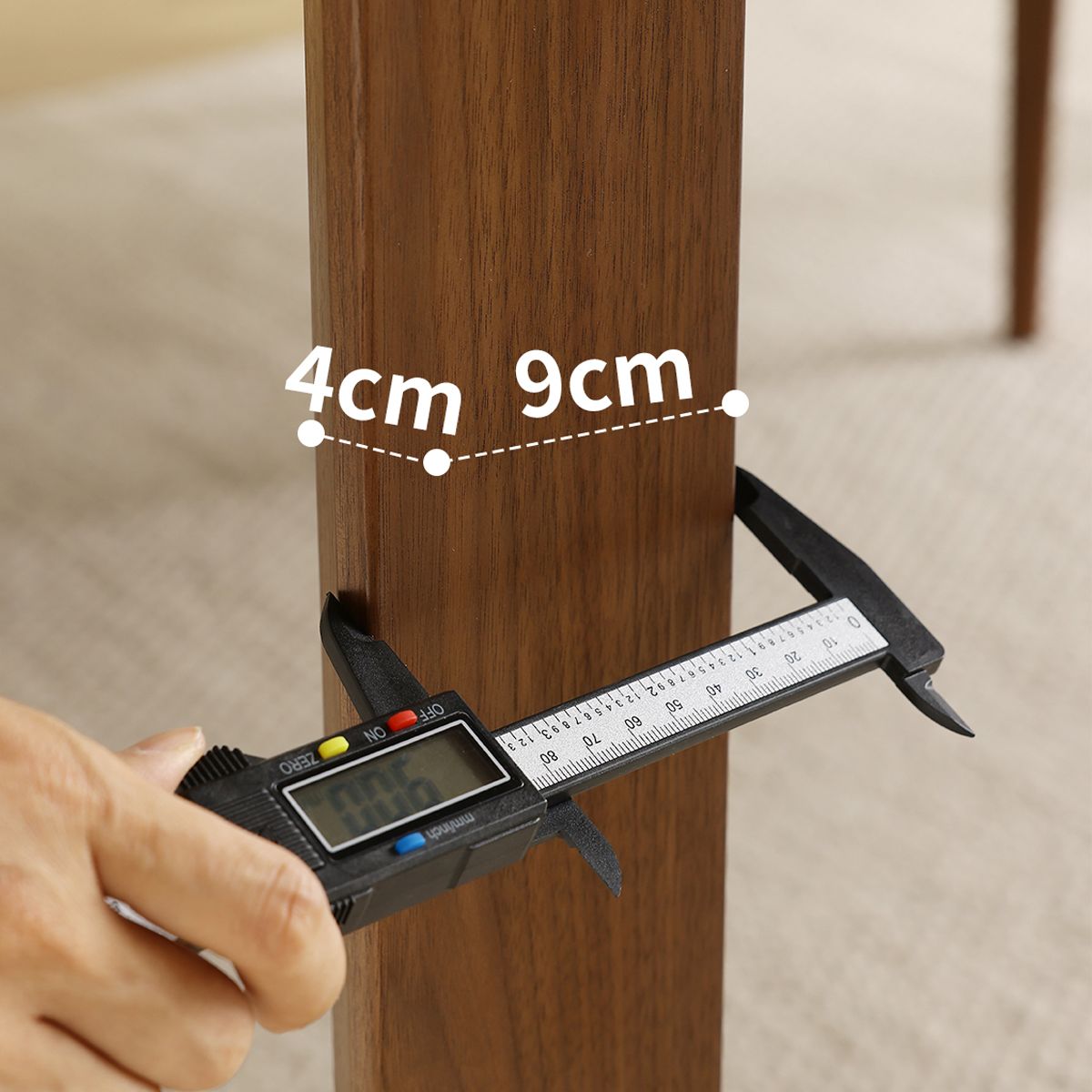 Hand using digital caliper to measure thickness of wooden table leg with 4cm and 9cm markings