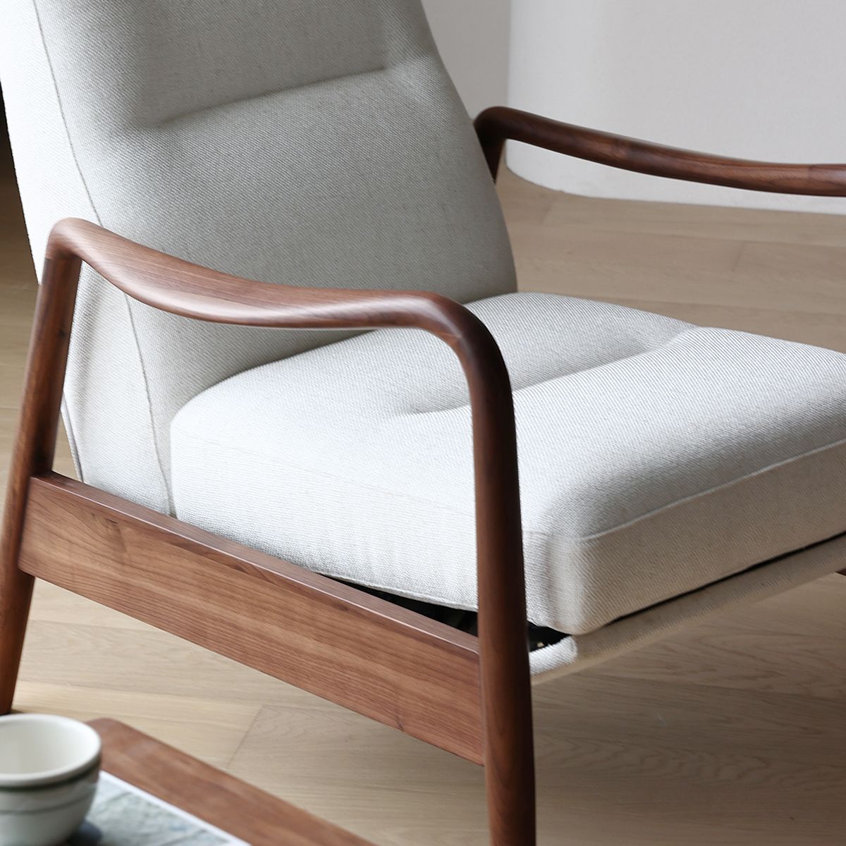 Modern lounge chair with white upholstery and smooth North American Black Walnut frame on light wood floor