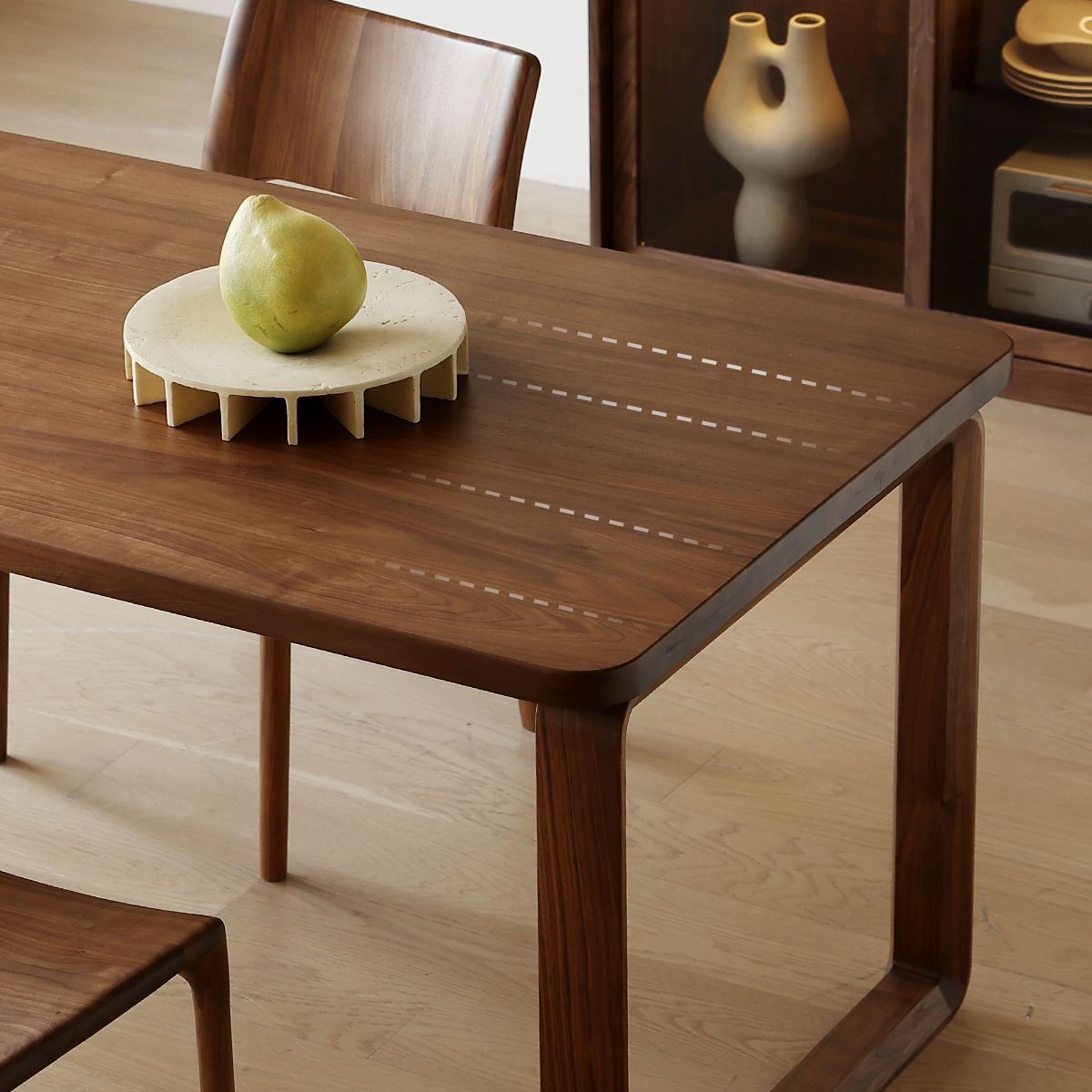 Modern wooden dining table with matching chairs, ceramic centerpiece, and pear in minimalist room