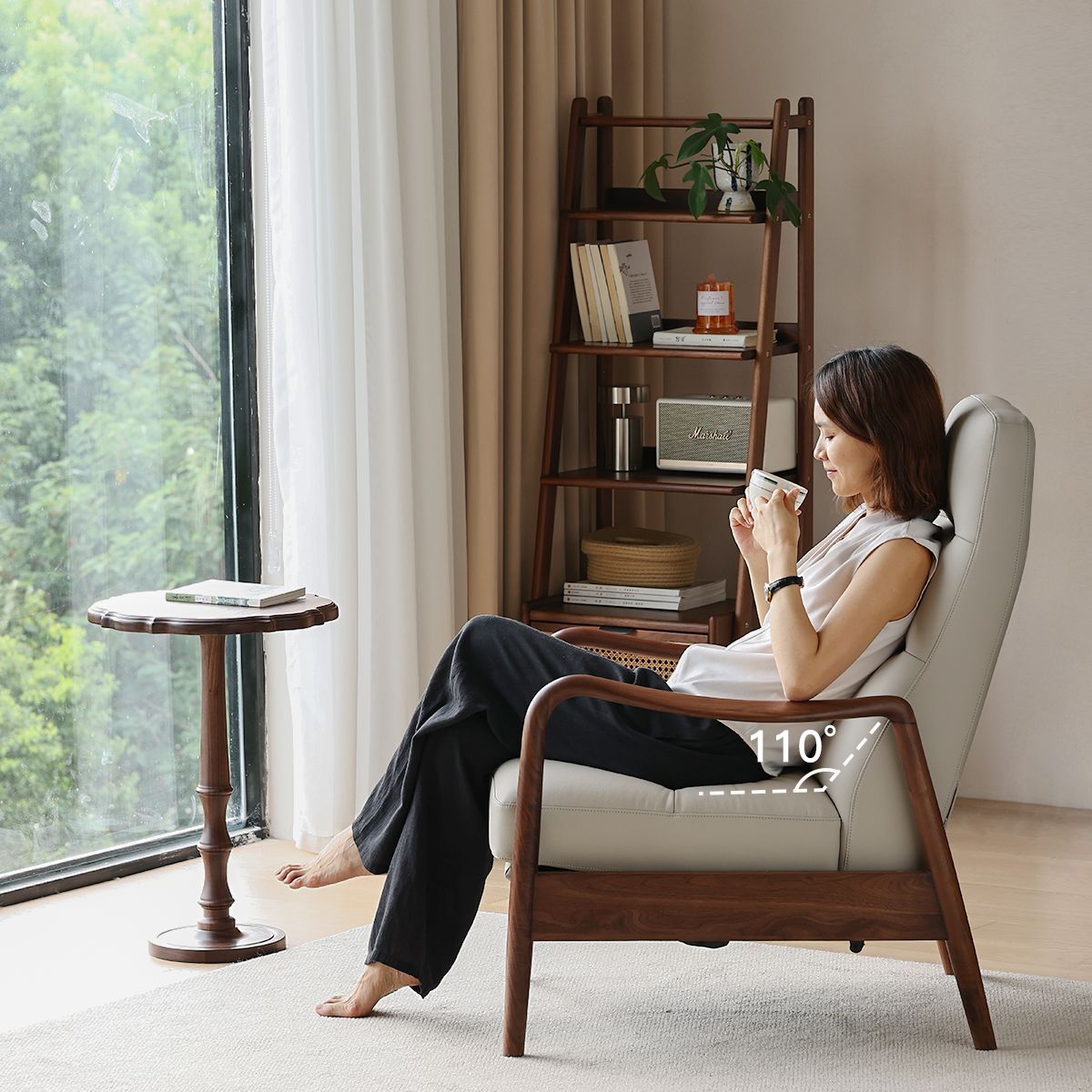 Woman relaxing in a walnut wood lounge chair with 110° recline, holding a cup by a window with natural light
