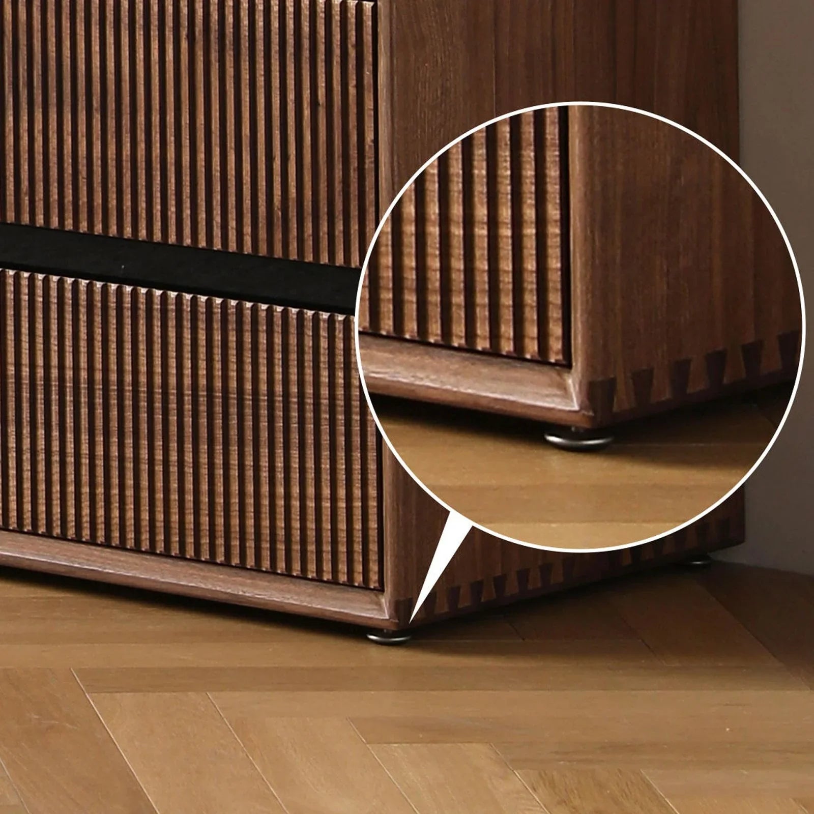 Close-up of wooden furniture corner with vertical grooves, dovetail joints, and small metal floor protector