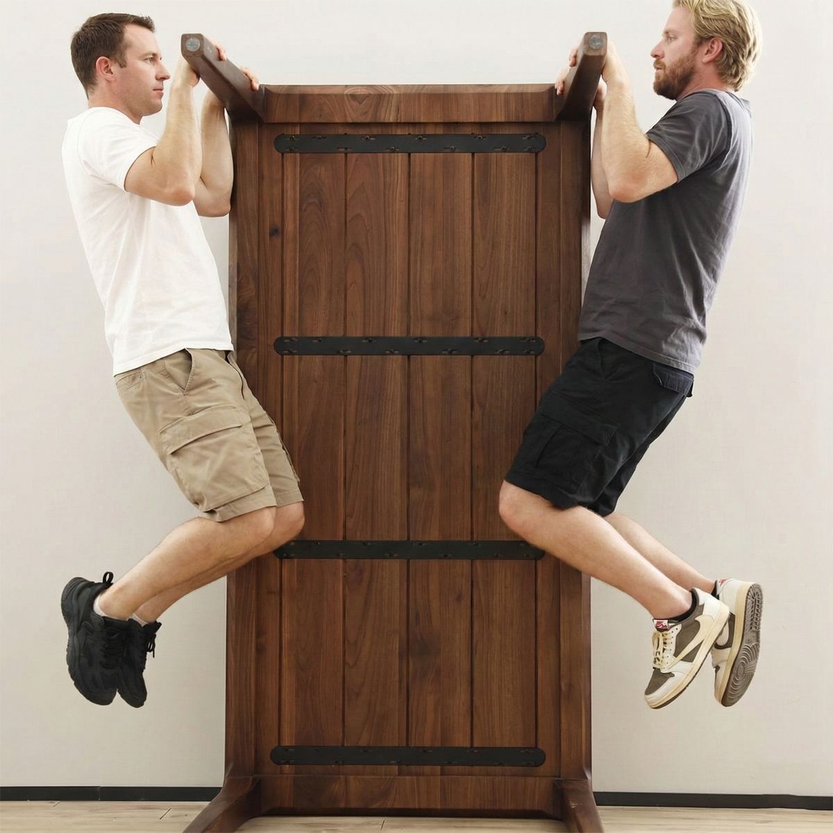 Two men doing pull-ups using an upside-down wooden table as a workout bar indoors