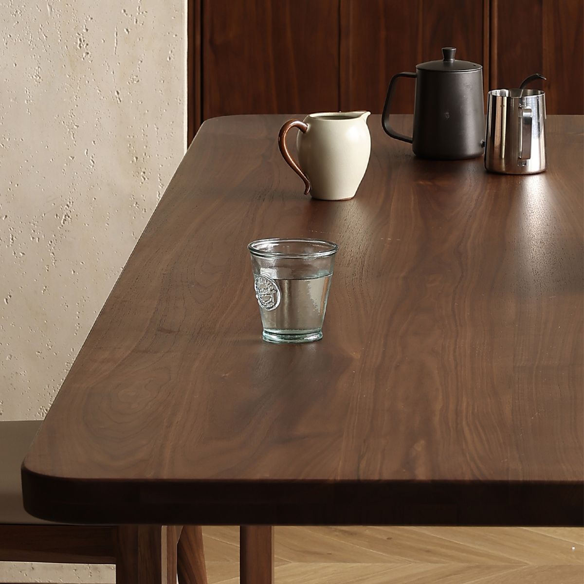 Wooden table with glass of water, ceramic jug, black teapot, and stainless steel milk frother