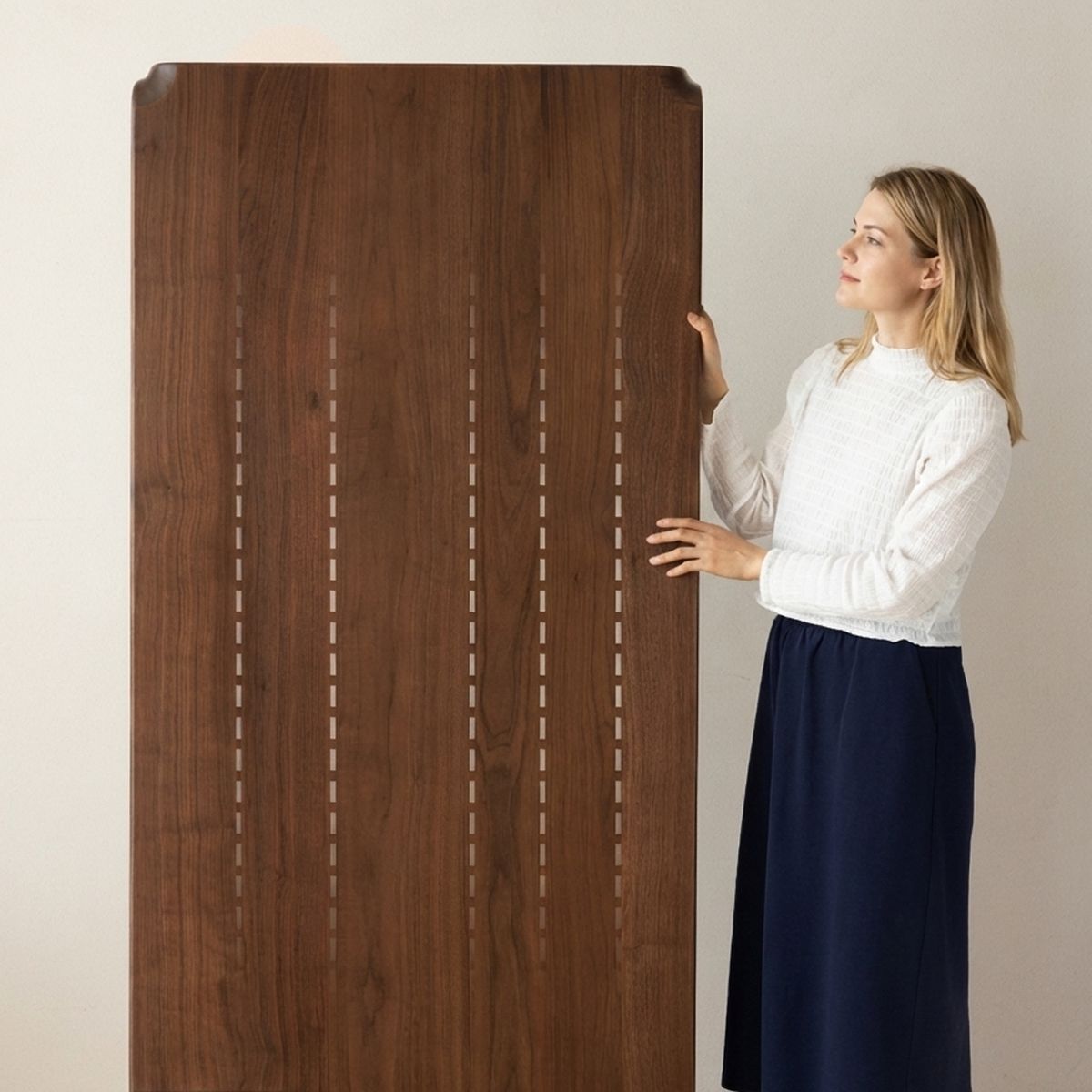 Woman in white top and navy skirt holding large wooden table with decorative inlay