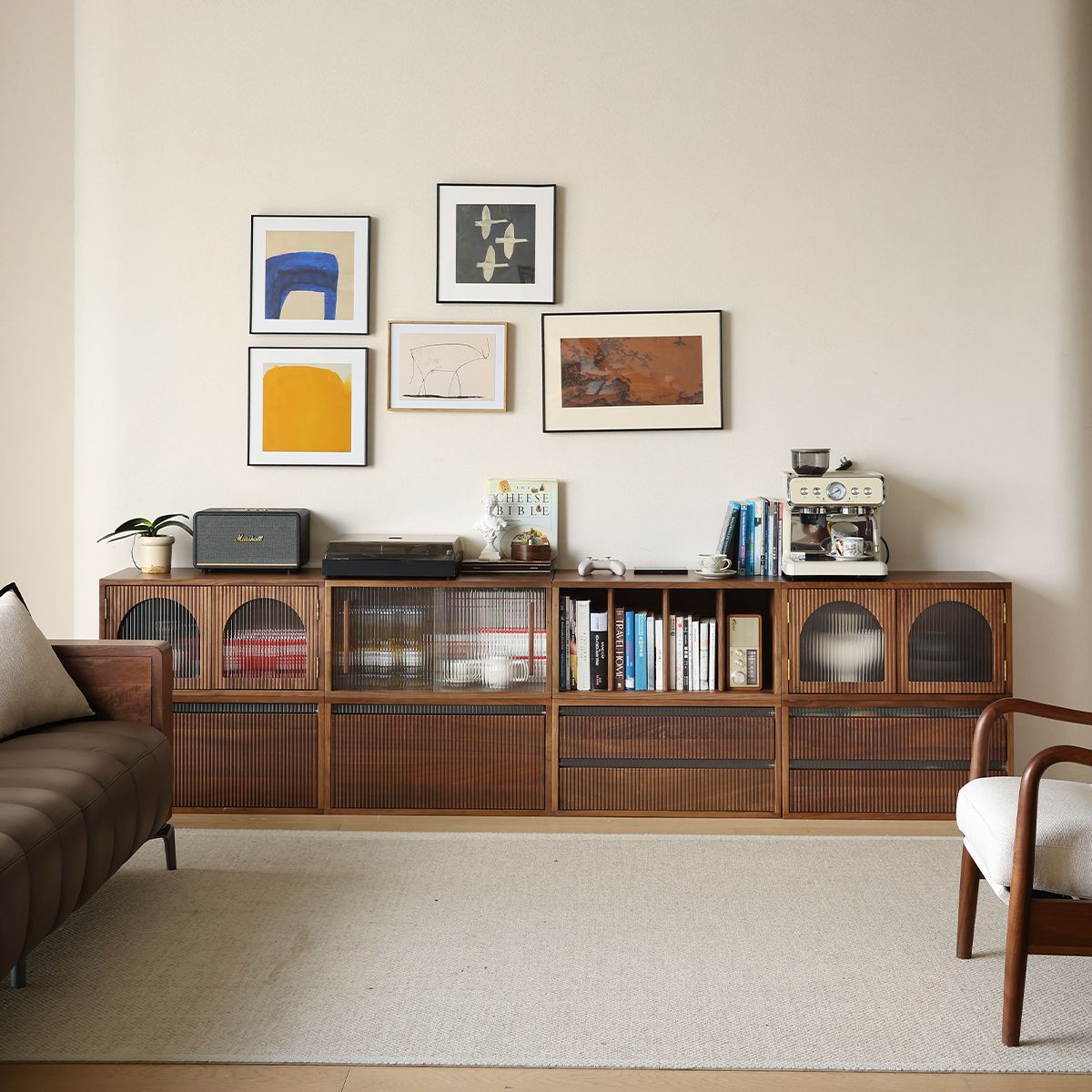 Minimalist living room with wooden cabinet, colorful abstract wall art, coffee machine, books, and cozy seating